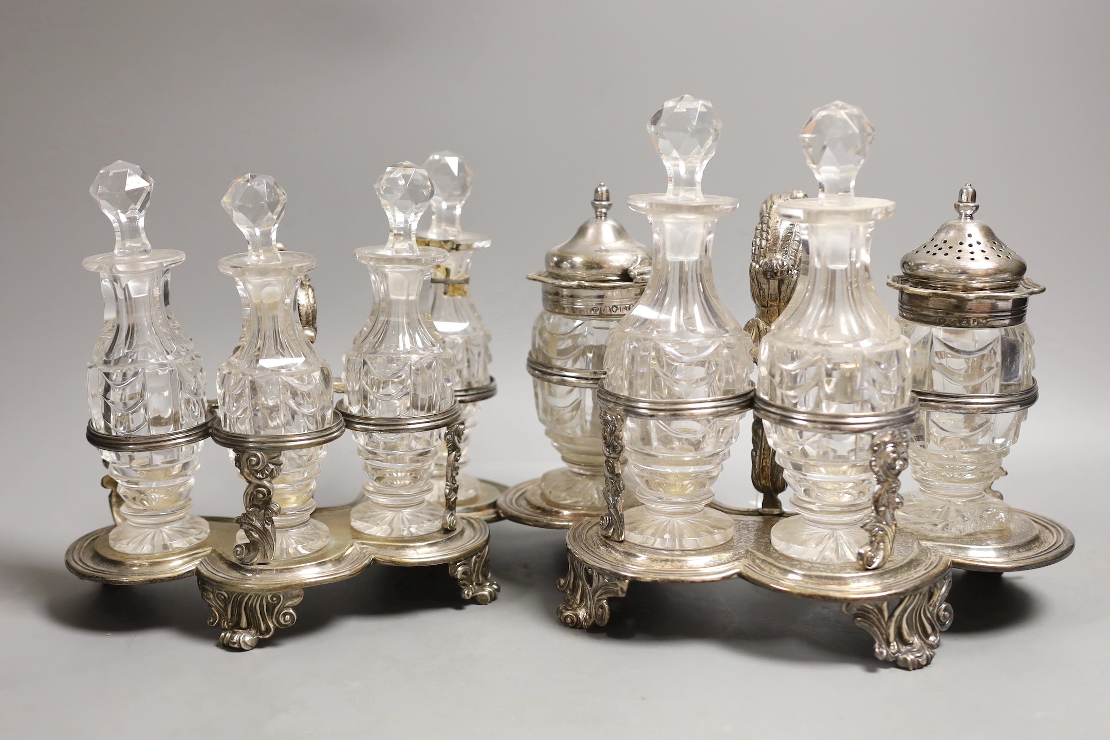 A graduated pair of William IV silver cruet stands, with ornate scroll handles, by John Fry II, London, 1830, both with four glass bottles, the largest with two silver mounted bottles, glass a.f., tallest 16cm, 34.3oz.